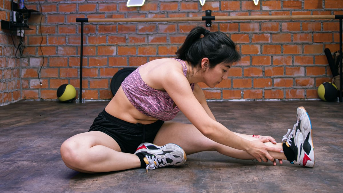 Woman performing stretches on gym floor, promoting exercise flexibility.